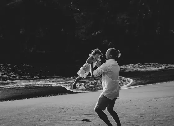 Ojciec podrzucający córkę w powietrze na plaży Abama Beach w czarno-białym ujęciu
