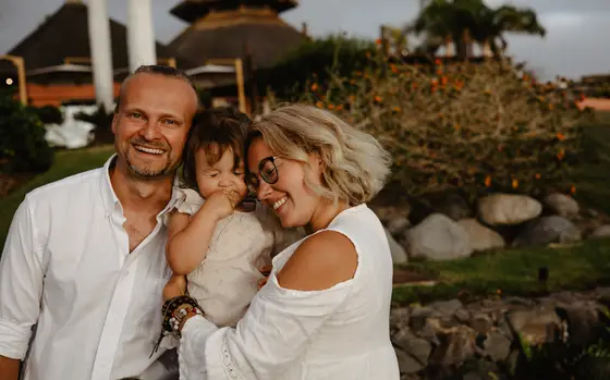 Rodzice uśmiechający się do siebie trzymając córkę w Abama Beach Resort