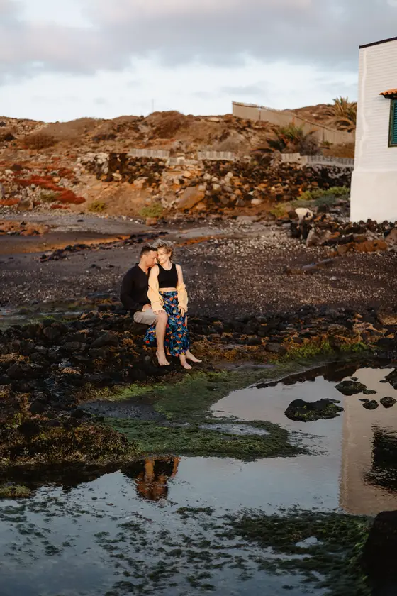 Couple sitting by natural pools with charming white beach house backdrop