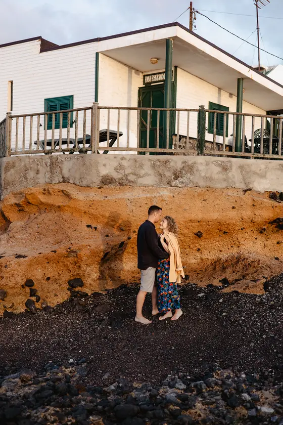 Lovers standing before white beach house on dramatic Tenerife volcanic coastline