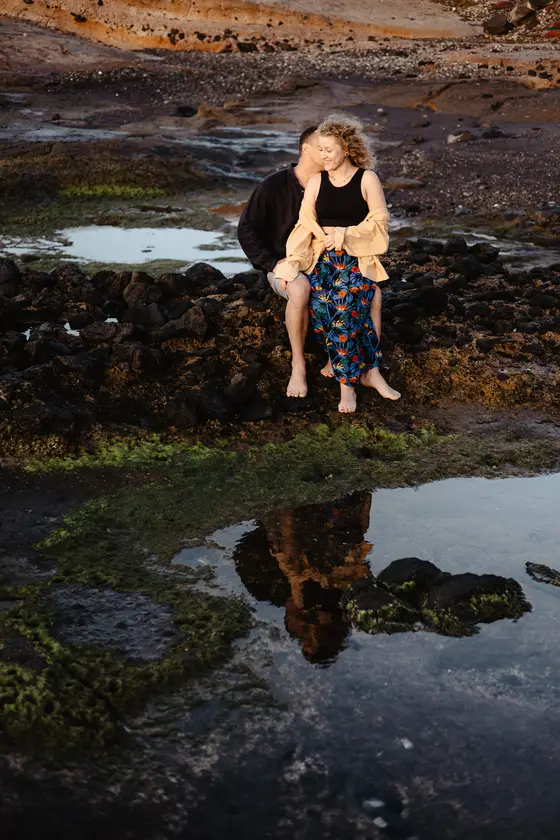 Romantic couple sitting on rocks with serene water reflections during sunset