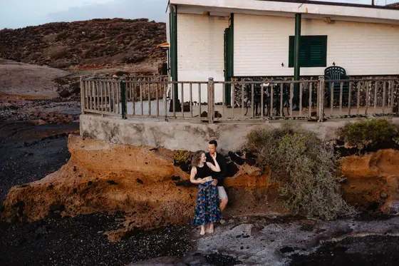Couple sitting on volcanic rocks during relaxed beach house photography session Tenerife