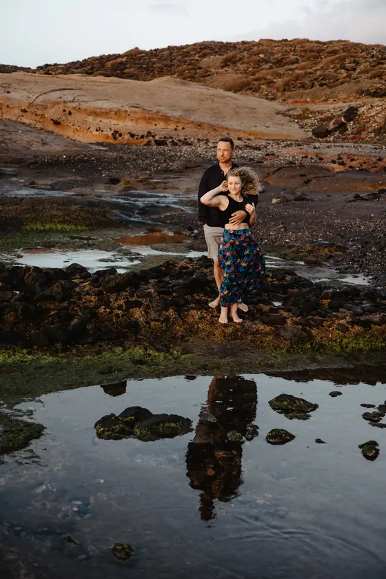 Tender couple embrace against dramatic volcanic landscape Tenerife with tide pool reflections