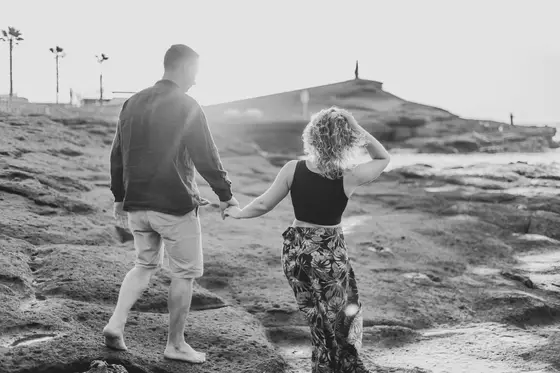 Couple walking along volcanic coastline holding hands in artistic black and white