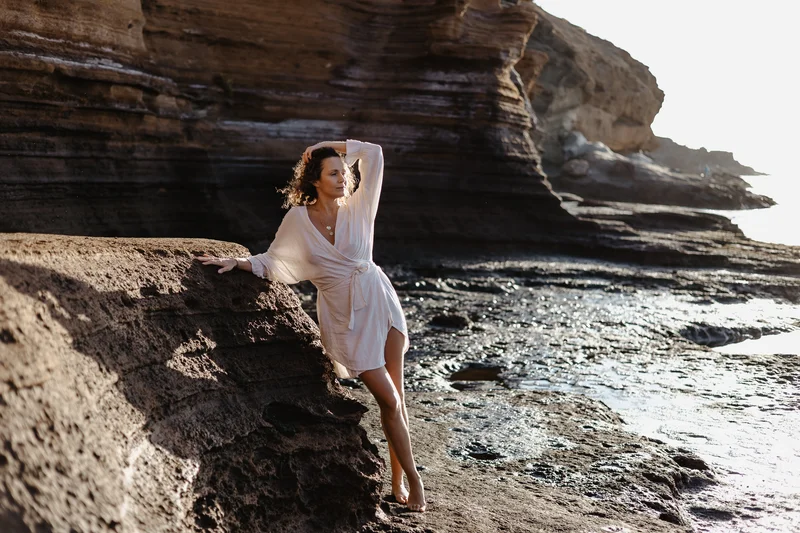 Monika Mrozowska en pose elegante en costa rocosa de Tenerife bajo luz solar cálida