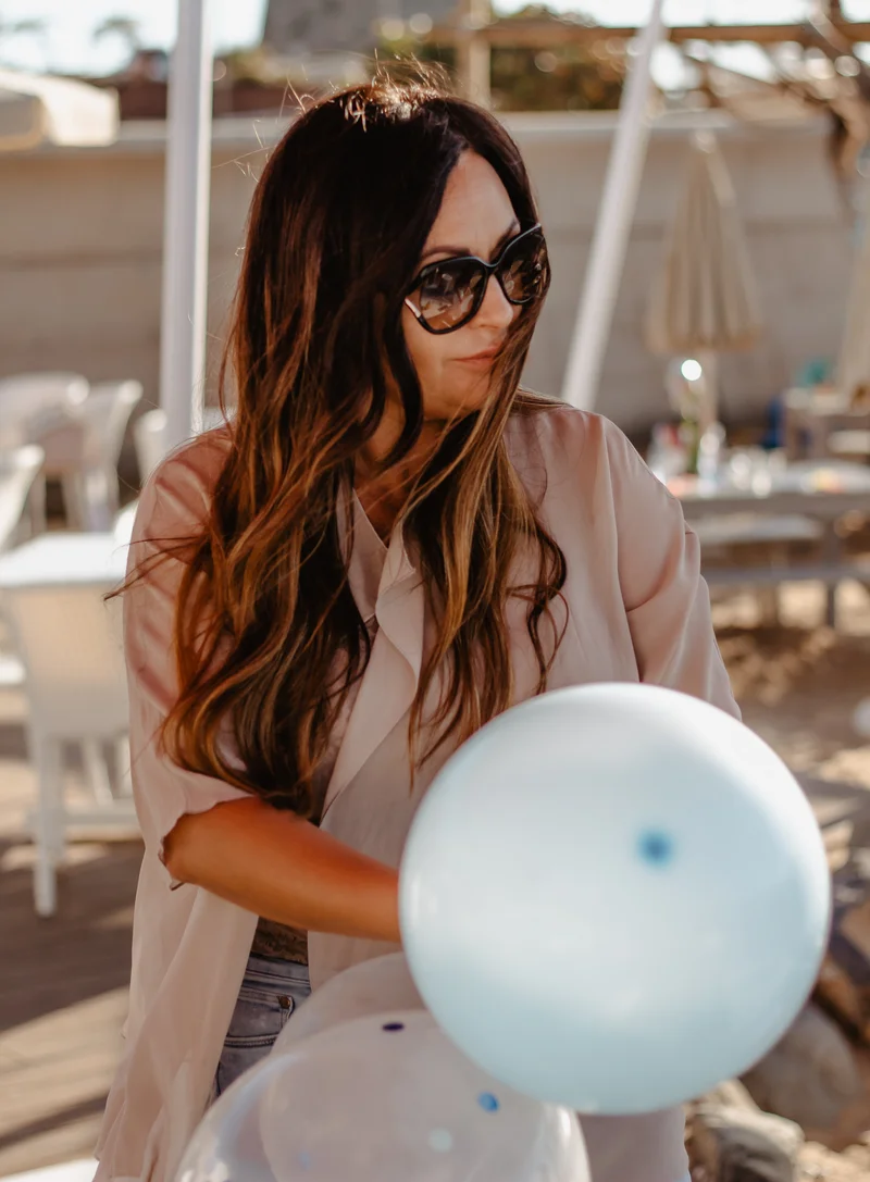 Brunette woman in sunglasses with blue balloon in warm afternoon light setting
