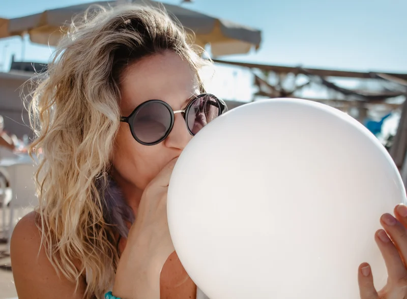 Blonde woman in sunglasses holding white balloon during professional event photo session