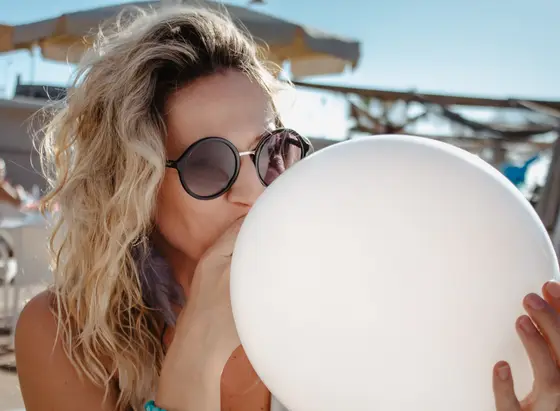 Blonde woman in sunglasses holding white balloon during professional event photo session