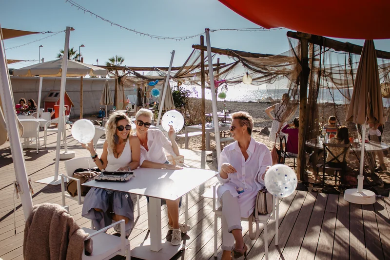 Group of female friends sitting at table with white balloons during party under canopies