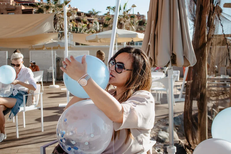 Woman in sunglasses blowing blue balloons during outdoor event party celebration