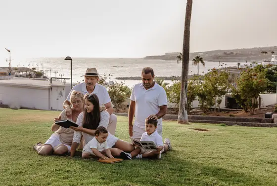 Retrato familiar multigeneracional sentados en césped del parque de Tenerife con palmeras