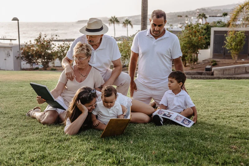 Multi-generational family reading book together on grass in Tenerife park