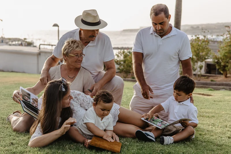 Grandmother, grandfather and grandchildren browsing photo album together on grass in Tenerife