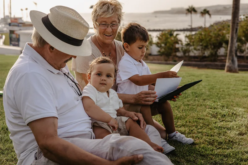 Grandparents with grandchildren reading book on grass in Tenerife park
