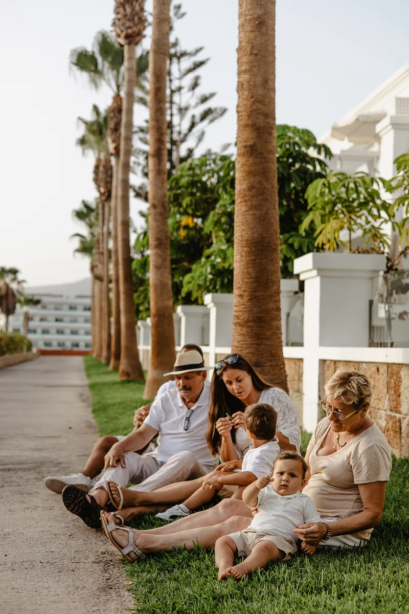 Family sitting under palm trees by white fence in Tenerife with mountain views