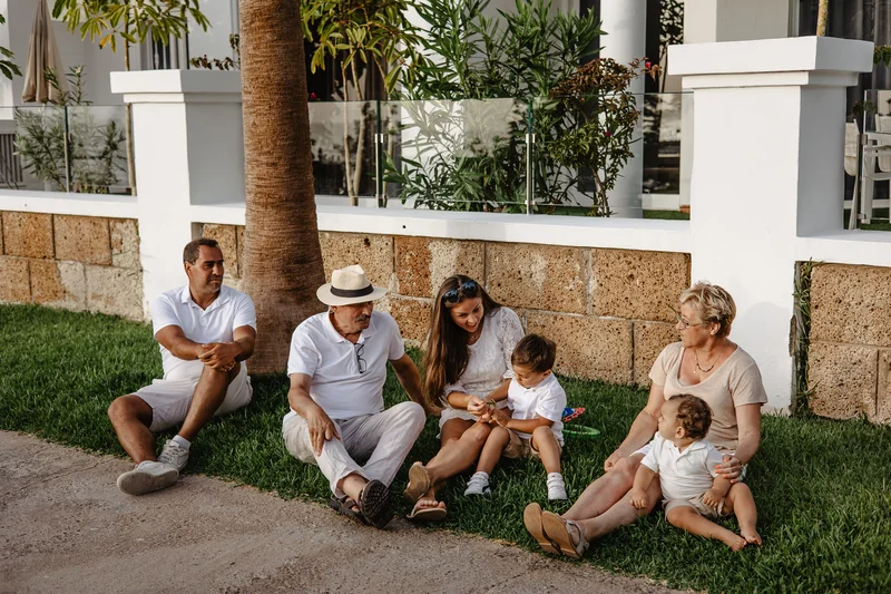 Multi-generational family sitting together on grass by palm trees in Tenerife