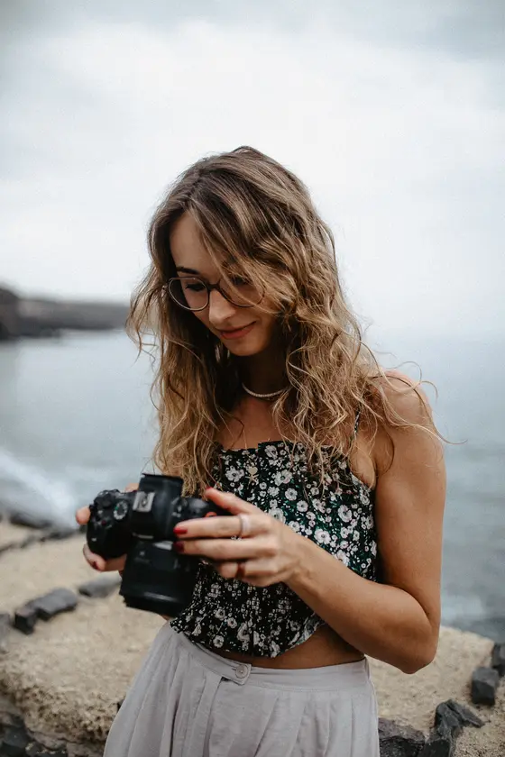 Mujer joven con pelo rizado sosteniendo cámara profesional en puerto marítimo de Tenerife