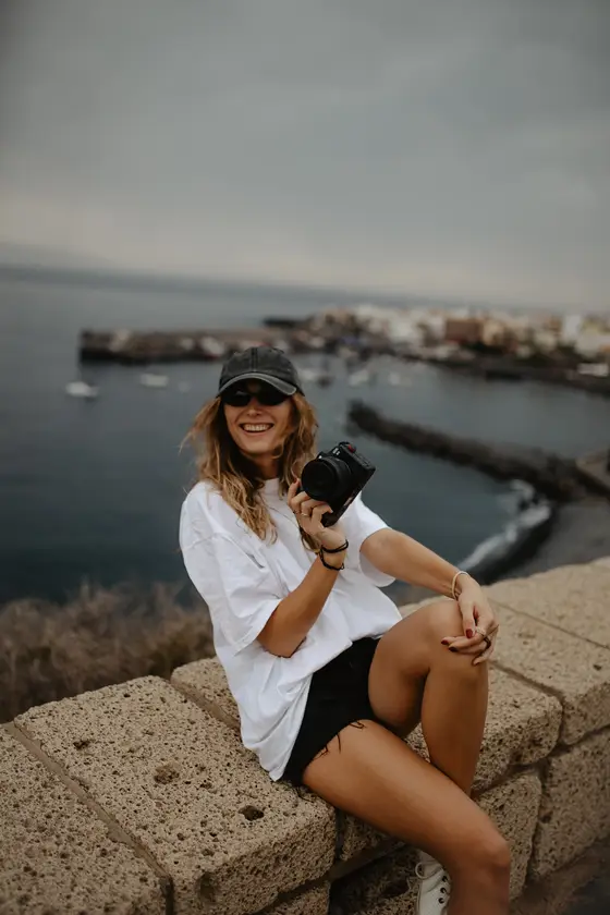 Fotógrafa profesional con cámara sentada en rocas costeras durante sesión fotográfica en Tenerife