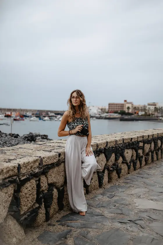 Mujer posando con cámara en paseo marítimo de piedra con barcos de fondo en Tenerife