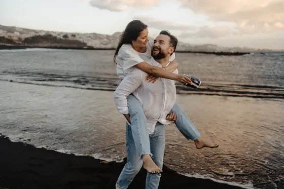 Couple in natural piggyback pose on beach during golden hour