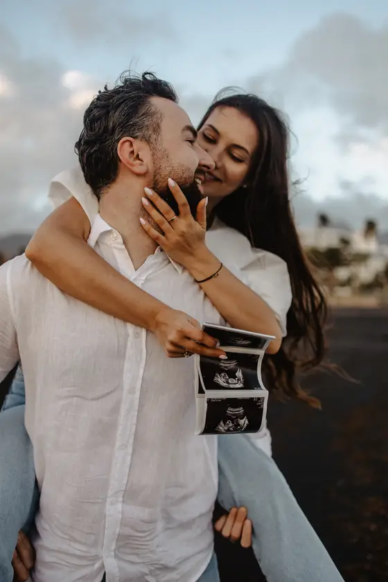Gentle forehead kiss of couple holding ultrasound photos during maternity session