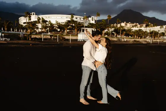 Romantic dancing pose of couple on volcanic beach with dramatic mountain backdrop