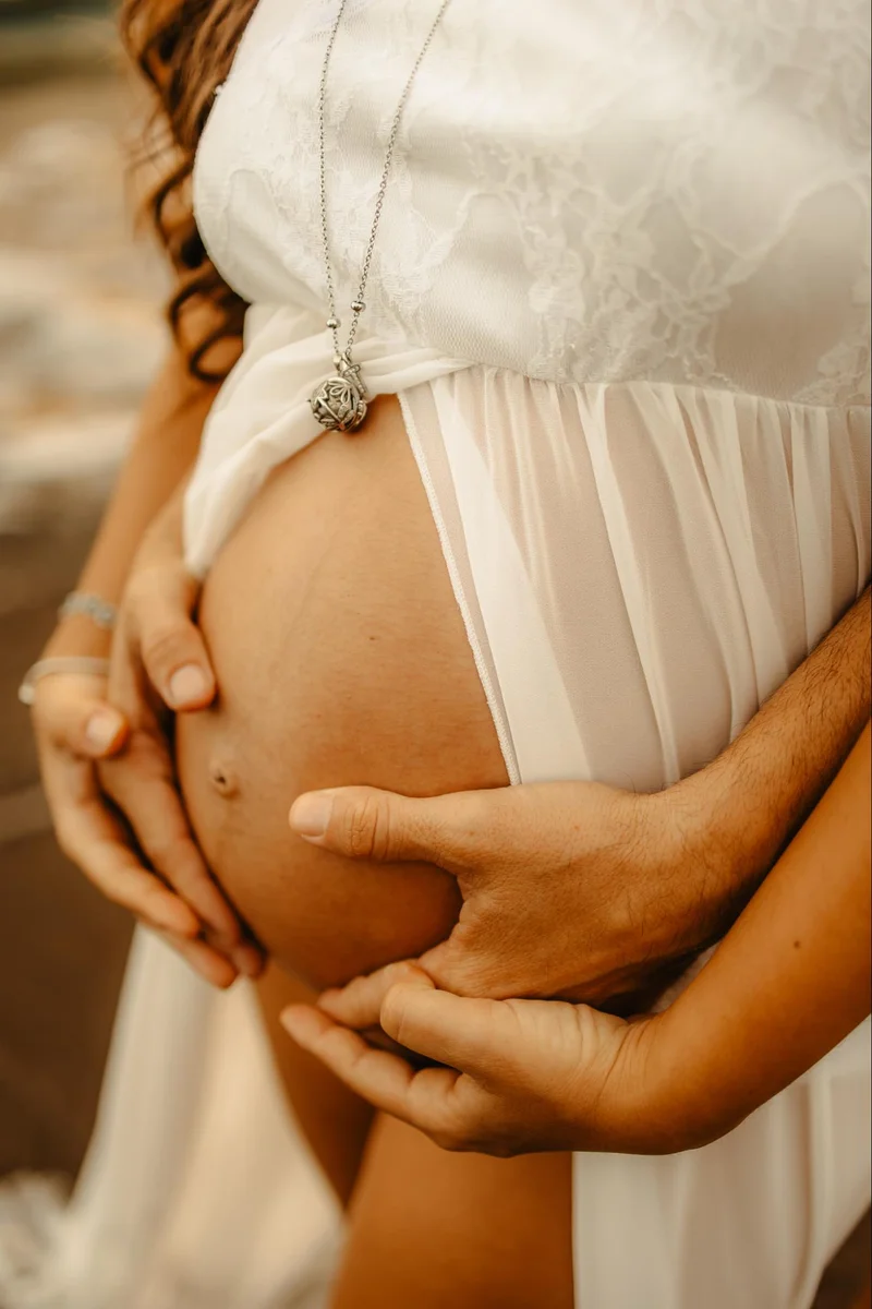 Close portrait of hands on a pregnant belly in a light dress