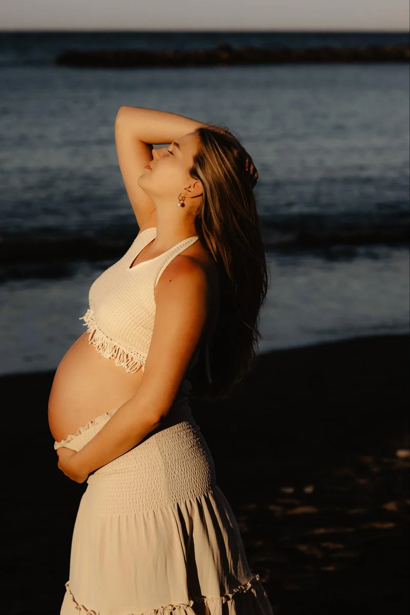 Pregnant woman standing by the ocean during golden hour