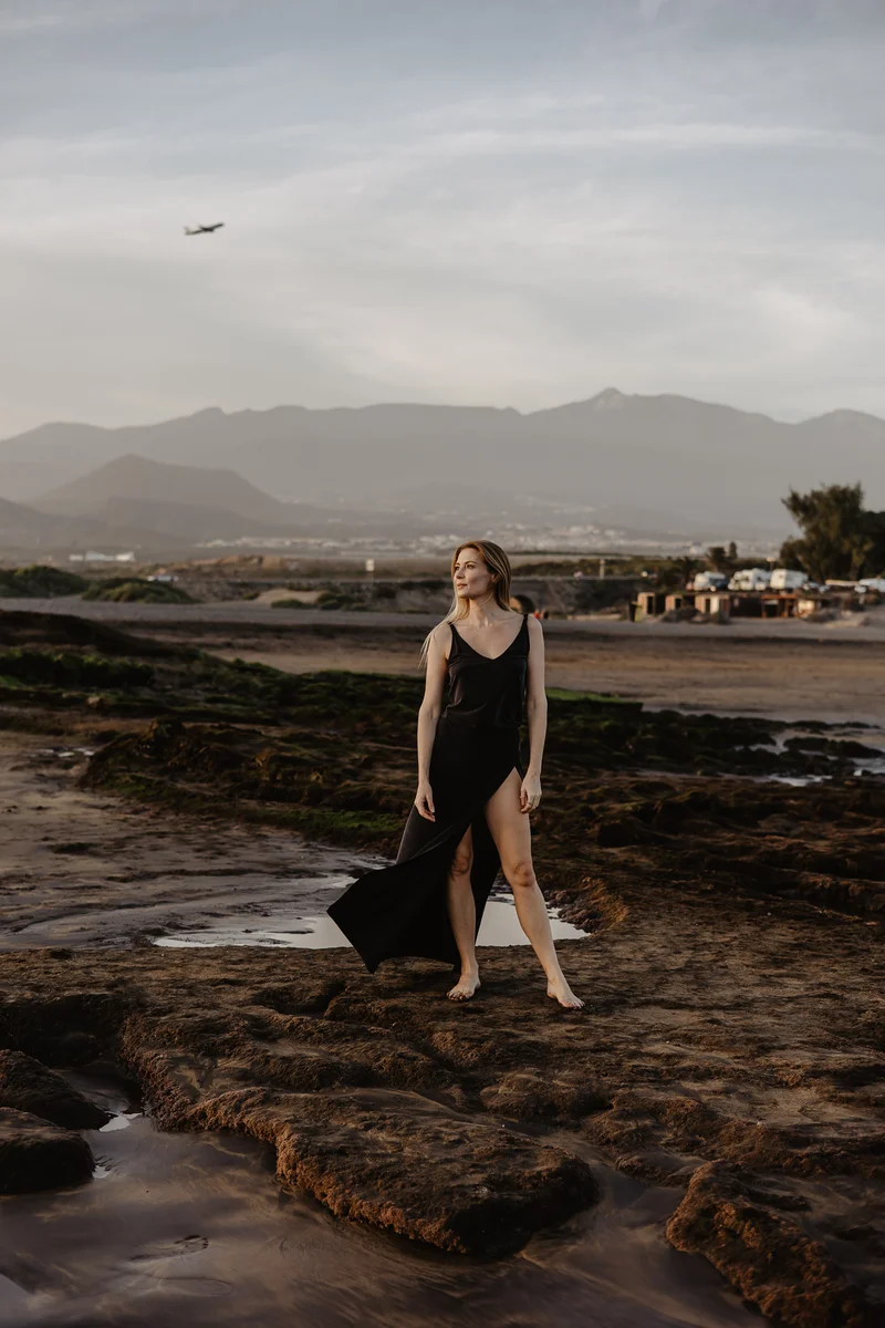 Karolina Chapko on dramatic rocky El Médano beach with airplane in sky and Tenerife mountains in background
