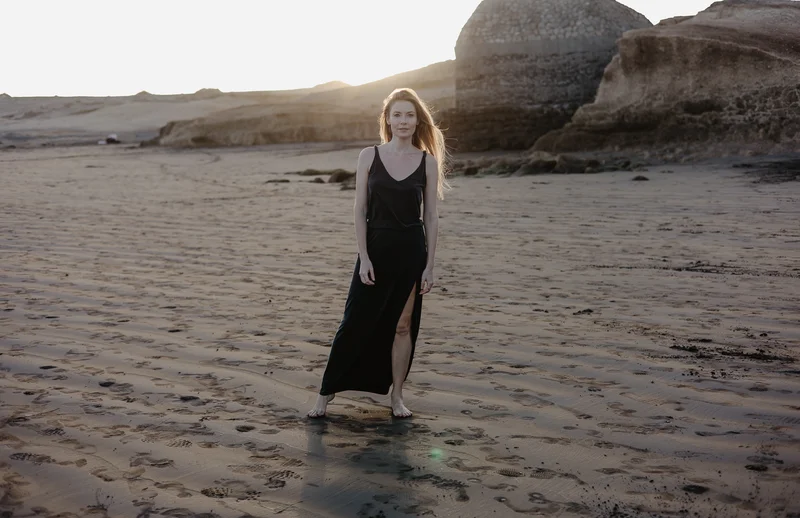 Karolina Chapko in long black dress walking on sandy El Médano beach during sunset