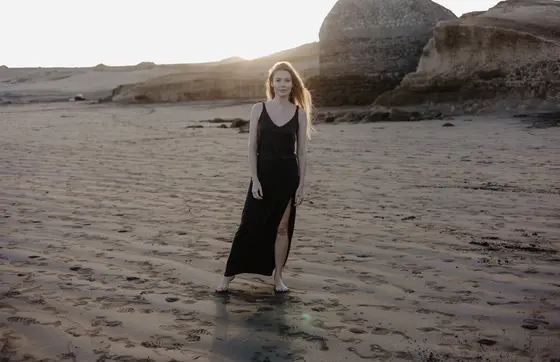 Karolina Chapko con vestido negro largo caminando en playa arenosa El Médano durante atardecer