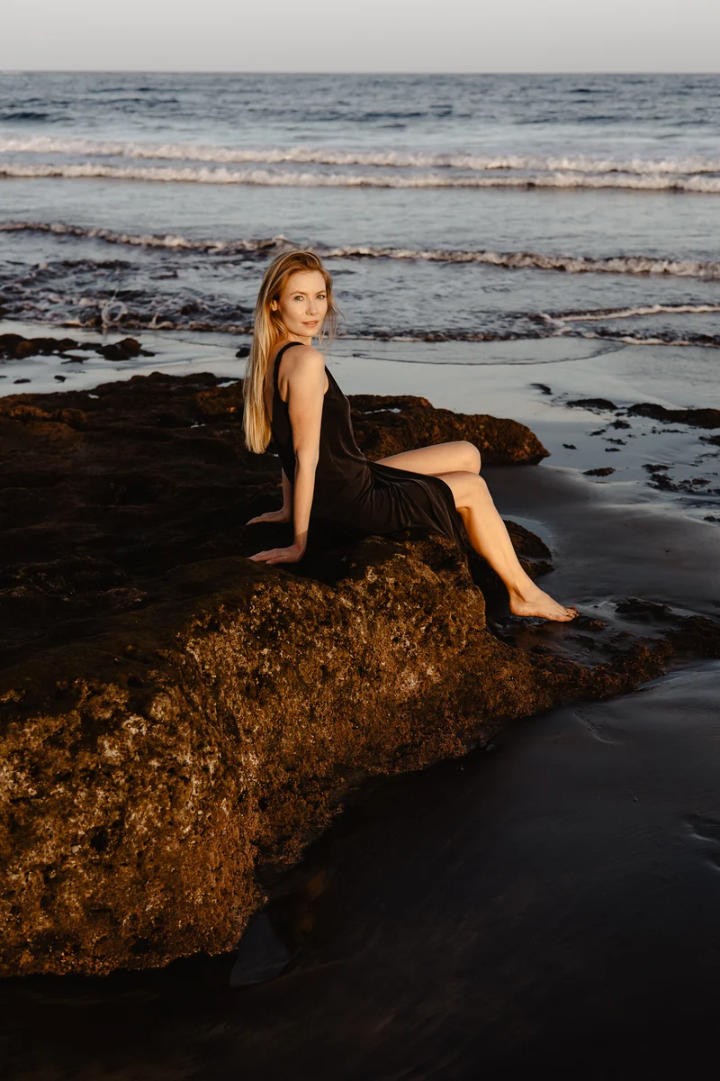 Karolina Chapko sitting on dark volcanic rocks of El Médano with ocean waves washing the shore