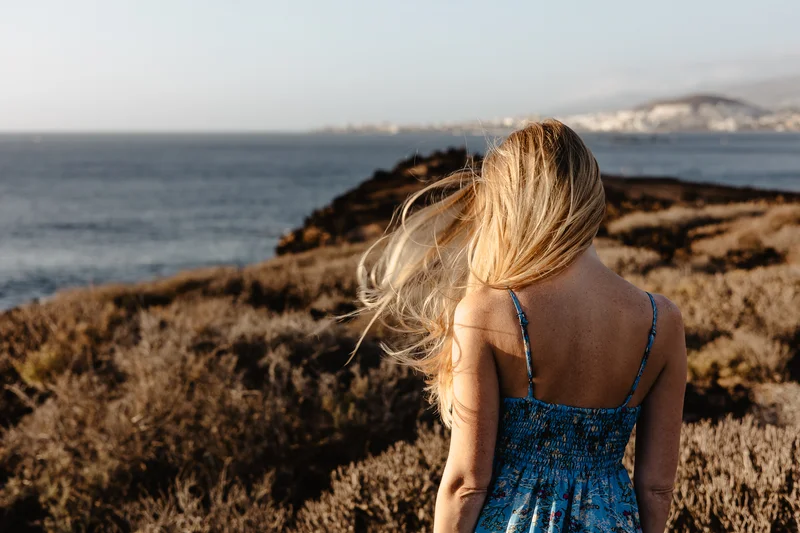 Retrato romántico de espaldas de Karolina Chapko con cabello al viento contemplando el océano en la costa de Tenerife