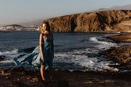 Portrait of Karolina Chapko in blue dress on rocky Tenerife coastline during golden hour