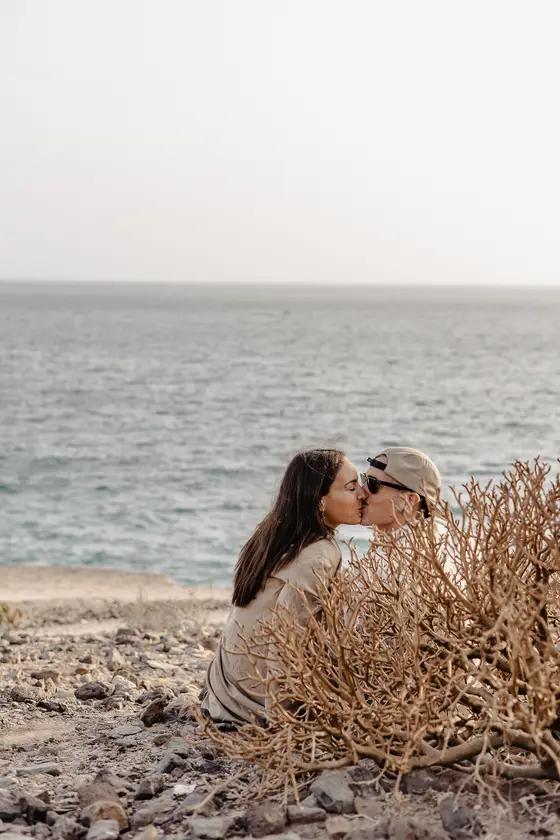 Pareja besándose románticamente entre plantas con telón de océano en La Caleta