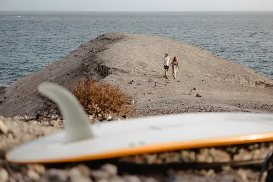 Pareja en la cima del acantilado de La Caleta con vista al océano y vegetación desértica