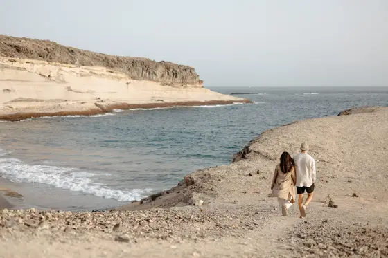 Pareja enamorada caminando por la orilla del océano en la playa La Caleta con formaciones rocosas