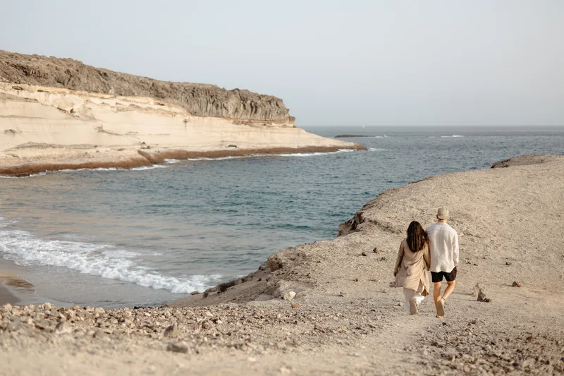 Pareja enamorada caminando por la orilla del océano en la playa La Caleta con formaciones rocosas