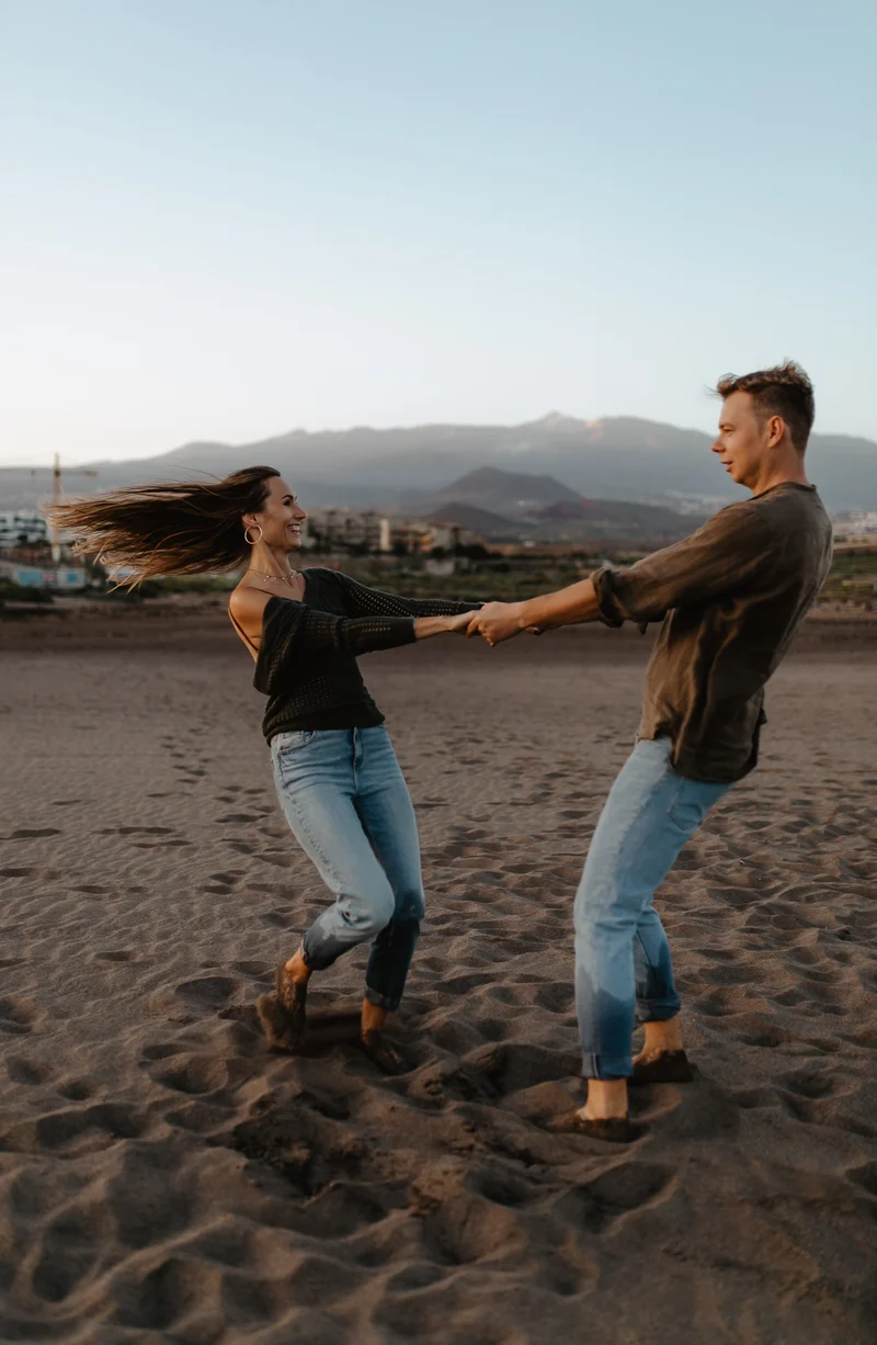 Pareja alegre girando tomada de las manos en playa La Tejita