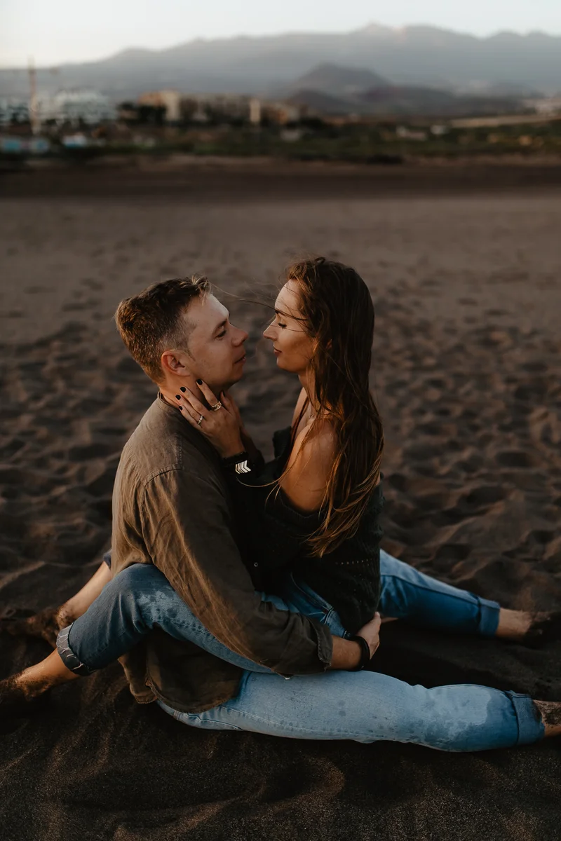 Beso romántico de pareja en playa La Tejita con montañas de fondo