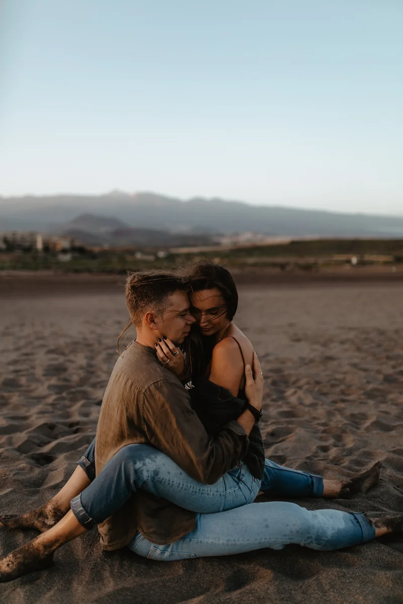Pareja sentada junta en arena oscura de playa La Tejita durante atardecer