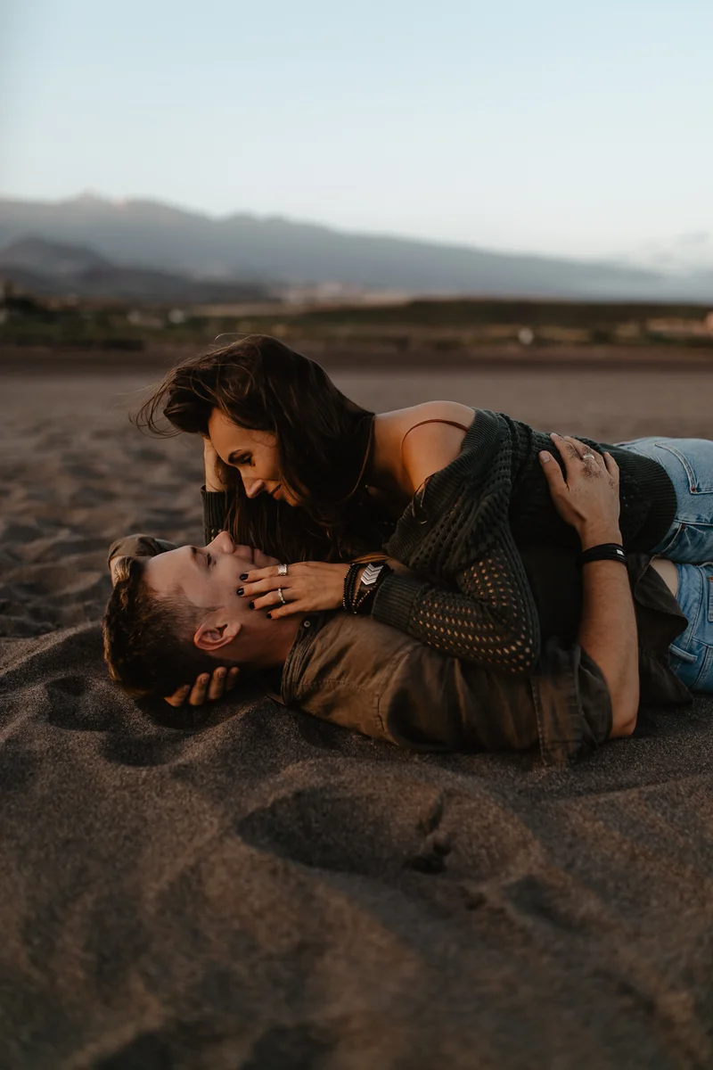Momento íntimo de pareja acostada en arena volcánica oscura en playa La Tejita