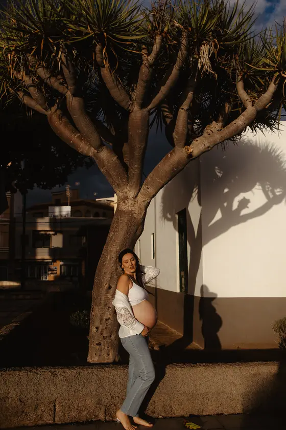 Mujer embarazada posando bajo palmera junto a arquitectura blanca en Tenerife durante sesión de maternidad