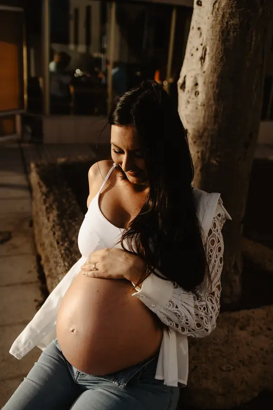 Mujer embarazada en vestido blanco posando a la sombra del árbol durante sesión íntima de maternidad en Las Galletas