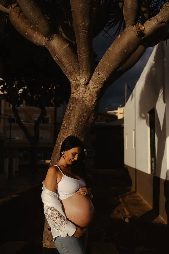 Futura madre en vestido blanco de encaje tocando vientre bajo palmera en el pueblo de Las Galletas