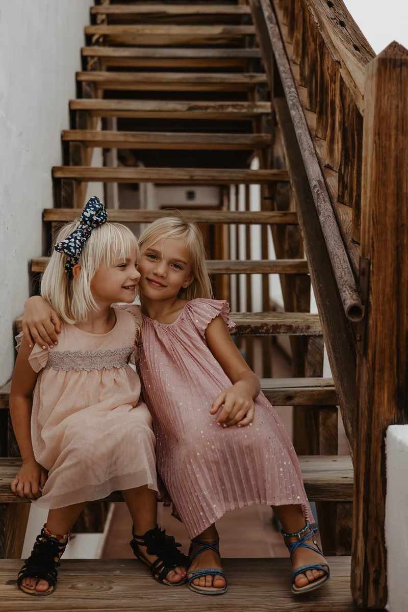 Two sisters in pink dresses cuddling on wooden stairs in Los Gigantes