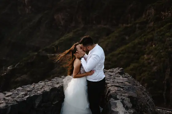Masca wedding photography intimate couple moment on stone cliff with mountain landscape backdrop