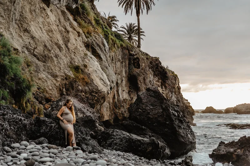 Expecting mother on rocky Tenerife beach with dramatic cliffs and palm trees backdrop