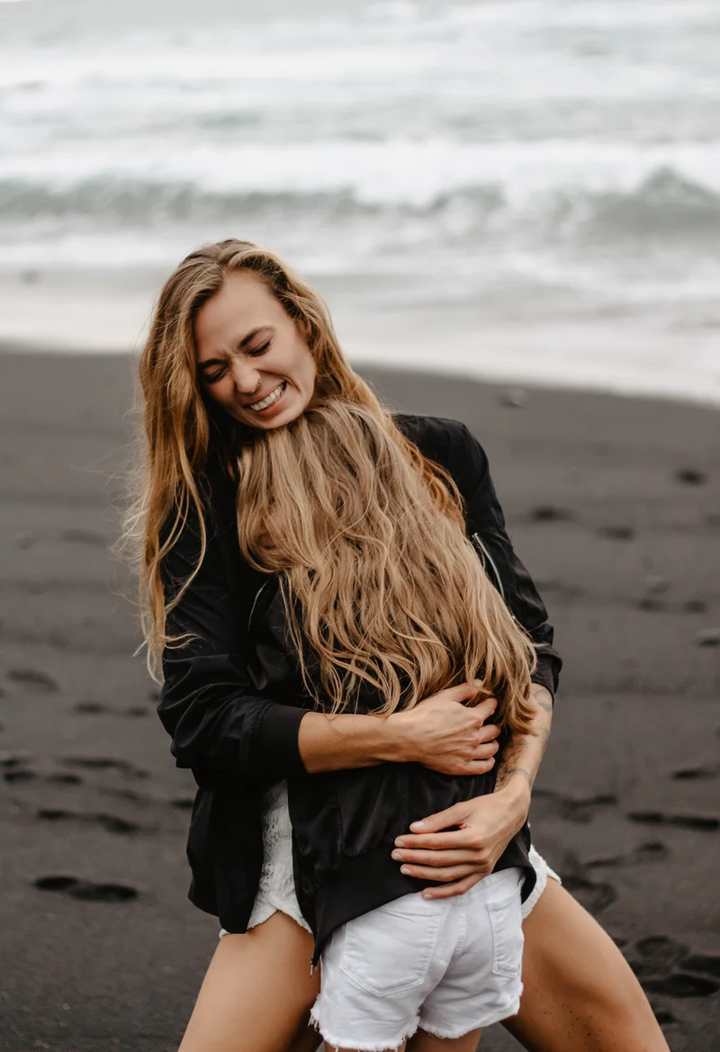 Tender embrace between mother and daughter on dark beach with ocean waves backdrop in Tenerife session