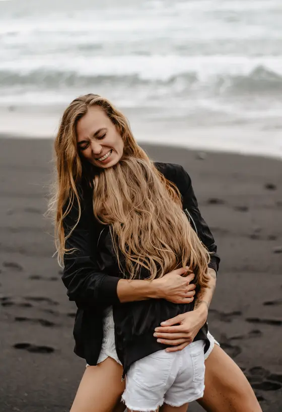 Tender embrace between mother and daughter on dark beach with ocean waves backdrop in Tenerife session